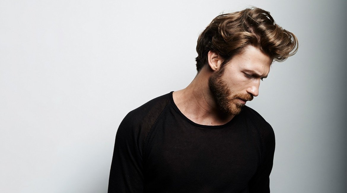 Junger Mann, blond, mit Vollbart schaut nachdenklich zur Seite